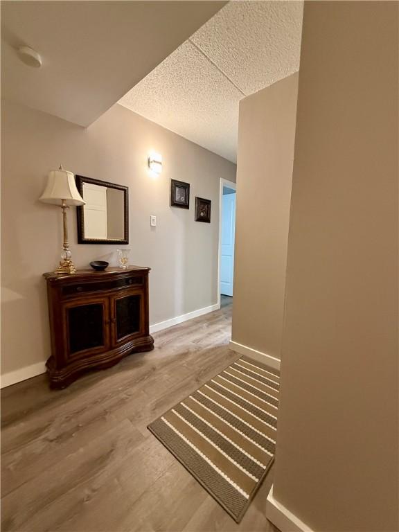 hallway featuring wood finished floors, baseboards, and a textured ceiling