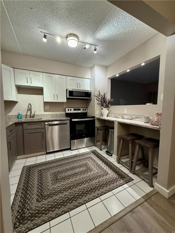 kitchen featuring stainless steel appliances, a sink, a textured ceiling, white cabinets, and light tile patterned floors