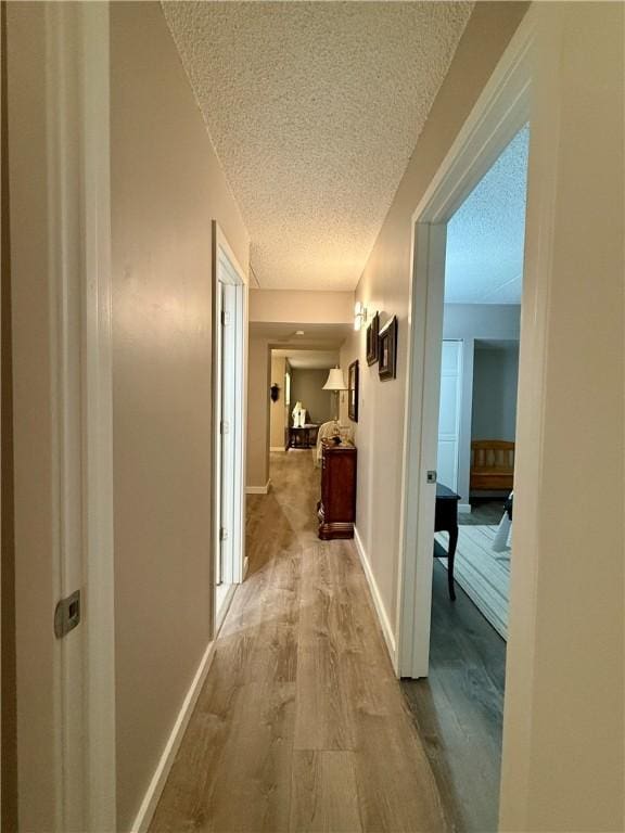 corridor with a textured ceiling, wood finished floors, and baseboards