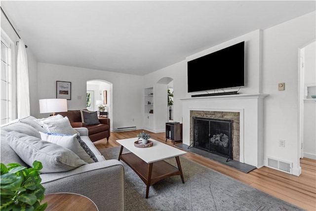 living area featuring arched walkways, wood finished floors, a baseboard heating unit, and plenty of natural light