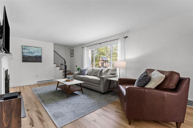 living room featuring a baseboard heating unit, stairway, light wood-type flooring, and a fireplace