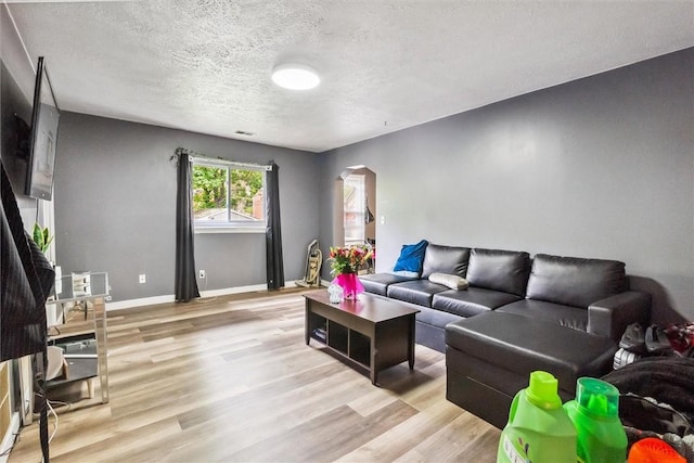 living area with arched walkways, light wood-style floors, a textured ceiling, and baseboards