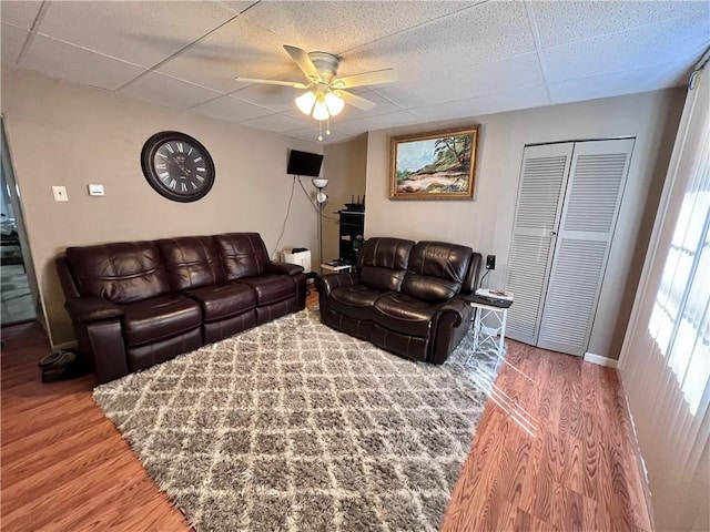 living area with wood finished floors, ceiling fan, and a paneled ceiling