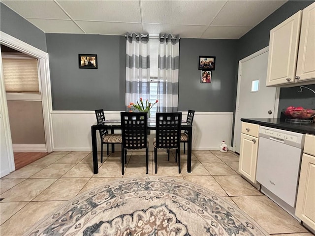 dining space with a drop ceiling, light tile patterned floors, and wainscoting