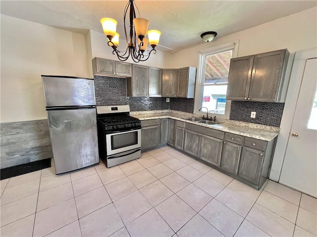kitchen featuring appliances with stainless steel finishes, a sink, a chandelier, light tile patterned floors, and pendant lighting