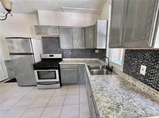 kitchen with appliances with stainless steel finishes, a sink, tasteful backsplash, and light tile patterned floors