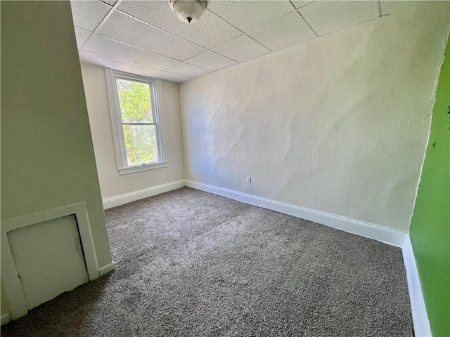 carpeted spare room featuring baseboards and a drop ceiling