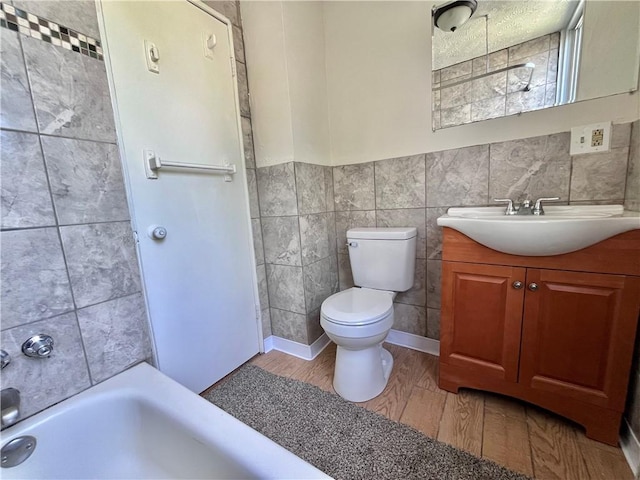 bathroom featuring a bath, toilet, wood finished floors, tile walls, and vanity