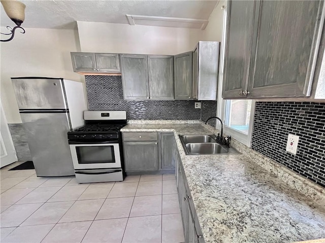 kitchen with appliances with stainless steel finishes, a sink, tasteful backsplash, and light tile patterned floors