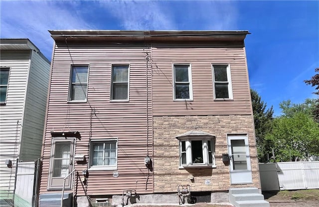 view of front of home featuring entry steps, stone siding, and fence