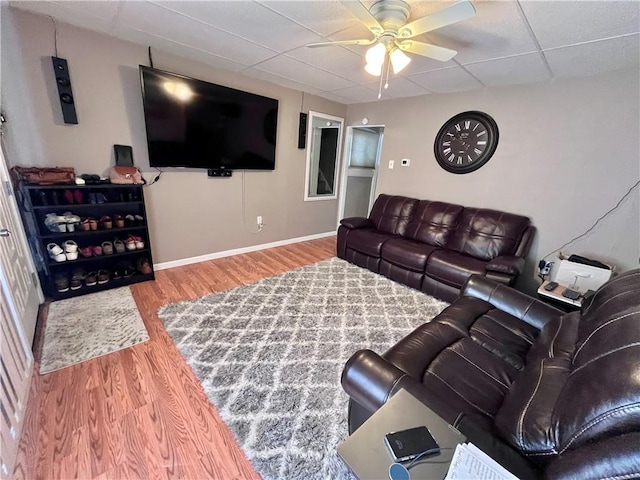 living room with a ceiling fan, wood finished floors, baseboards, and a paneled ceiling