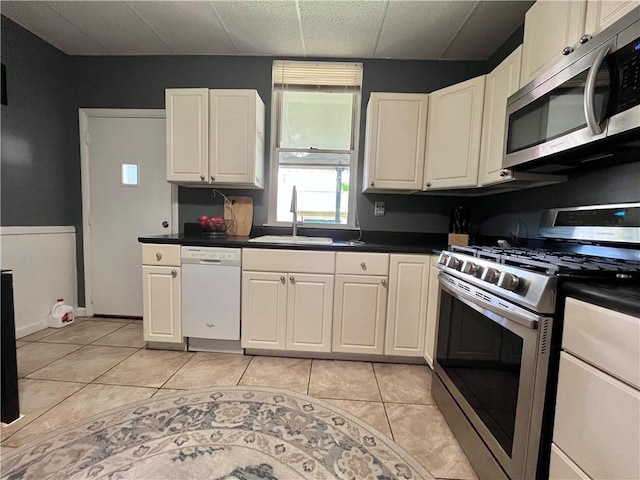 kitchen with appliances with stainless steel finishes, a sink, dark countertops, light tile patterned floors, and a drop ceiling