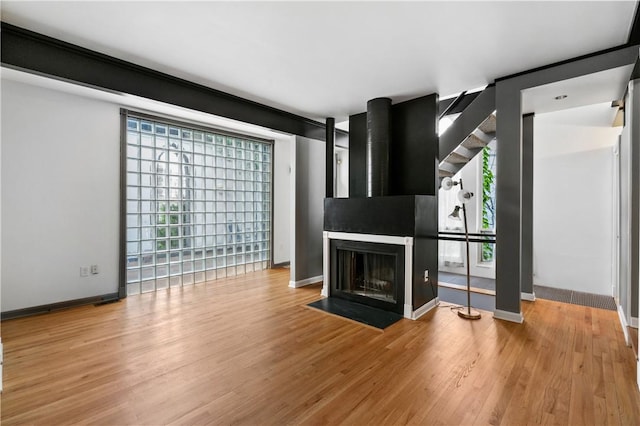unfurnished living room featuring wood finished floors, baseboards, and a multi sided fireplace