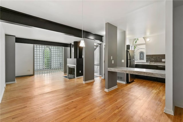 kitchen with freestanding refrigerator, light wood-type flooring, hanging light fixtures, baseboards, and a kitchen breakfast bar