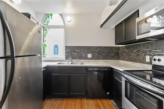 kitchen with appliances with stainless steel finishes, a sink, light wood-style flooring, light stone countertops, and backsplash