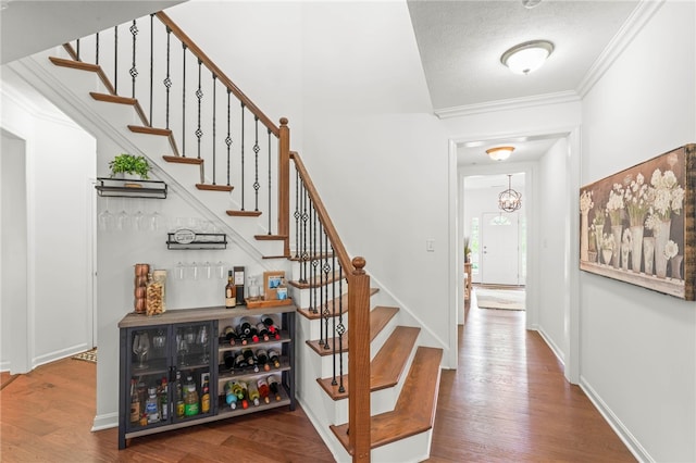entryway featuring stairway, wood finished floors, crown molding, a chandelier, and baseboards