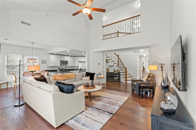 living area featuring ceiling fan, stairway, hardwood / wood-style floors, a high ceiling, and baseboards