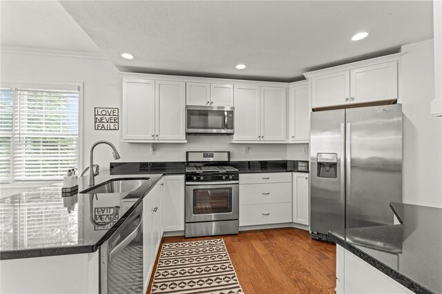 kitchen with stainless steel appliances, a sink, white cabinets, crown molding, and a peninsula