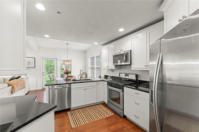 kitchen with appliances with stainless steel finishes, a sink, a peninsula, dark countertops, and recessed lighting