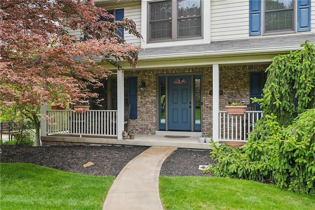 view of exterior entry with a porch and brick siding