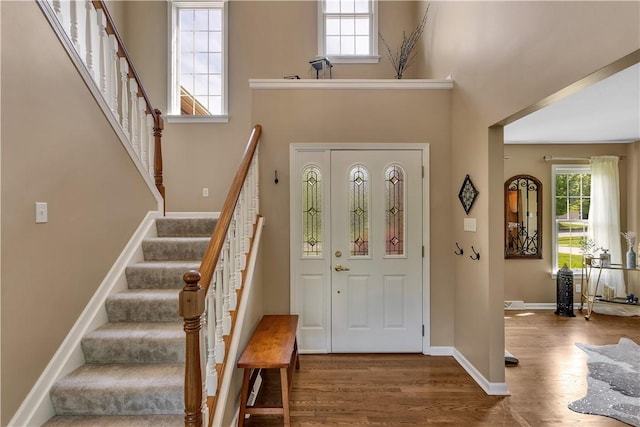 entrance foyer featuring wood finished floors, stairs, baseboards, and a towering ceiling