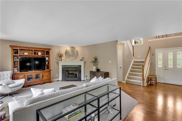 living room with stairs, wood finished floors, baseboards, and a tiled fireplace