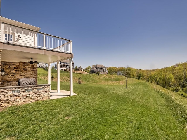 view of grassy yard featuring a balcony, a ceiling fan, and a patio