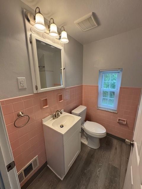 bathroom with tile walls, a wainscoted wall, wood finished floors, toilet, and vanity