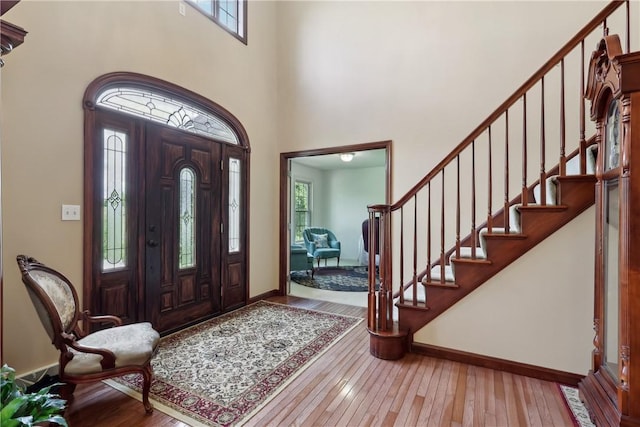 foyer with healthy amount of natural light, hardwood / wood-style floors, baseboards, and a towering ceiling