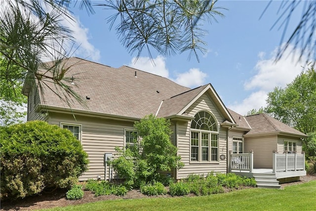 rear view of property featuring a deck, a lawn, and roof with shingles