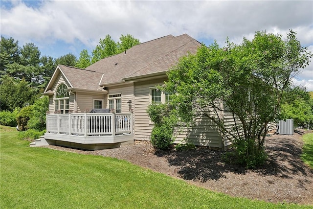 back of property with a lawn, a deck, a shingled roof, and central AC unit