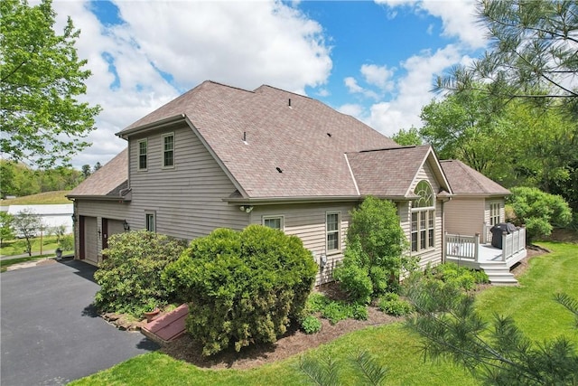 view of property exterior featuring driveway, roof with shingles, a deck, and a garage