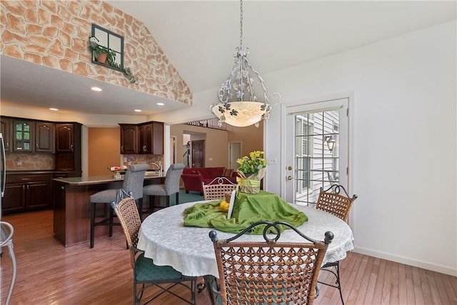 dining area with light wood-type flooring, baseboards, and high vaulted ceiling