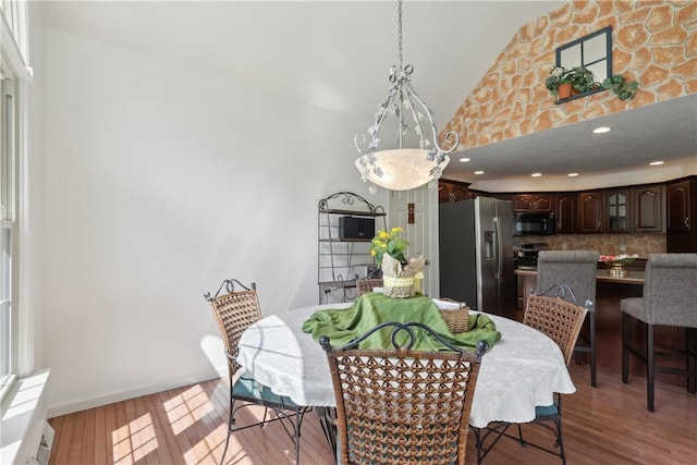 dining space featuring light wood-style flooring, high vaulted ceiling, and baseboards