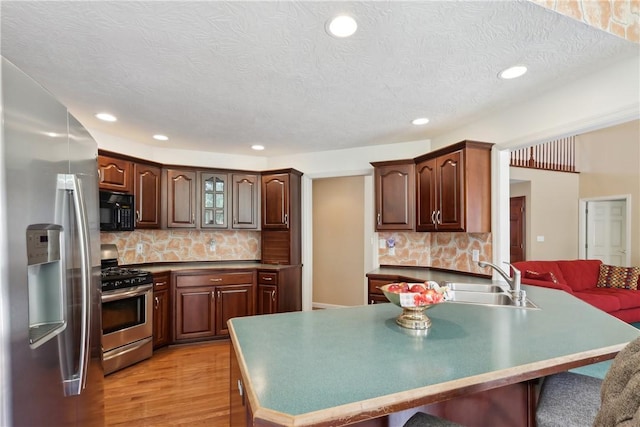 kitchen featuring appliances with stainless steel finishes, a sink, a breakfast bar area, light wood-type flooring, and backsplash