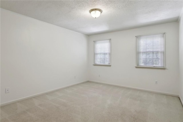 spare room with light colored carpet, baseboards, and a textured ceiling