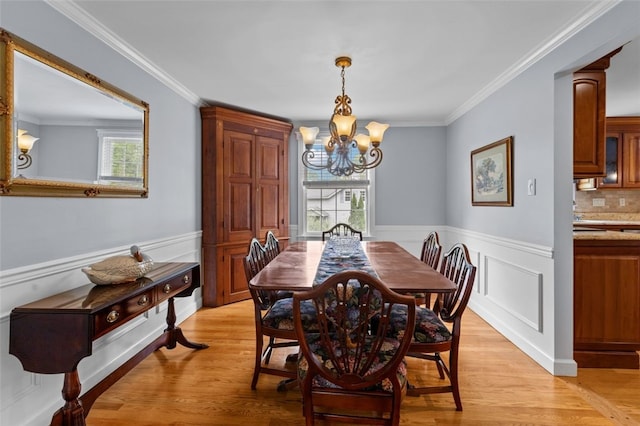 dining space featuring a chandelier, wainscoting, crown molding, and light wood-style floors