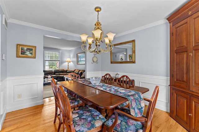 dining space featuring a chandelier, light wood-style flooring, a wainscoted wall, crown molding, and a decorative wall