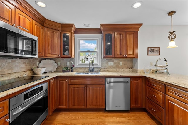 kitchen with stainless steel appliances, a sink, light stone countertops, light wood-style flooring, and brown cabinetry