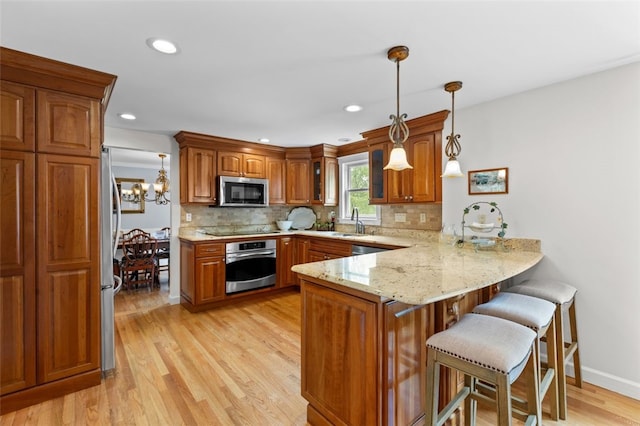 kitchen featuring stainless steel appliances, a peninsula, brown cabinets, a sink, and light wood-style floors