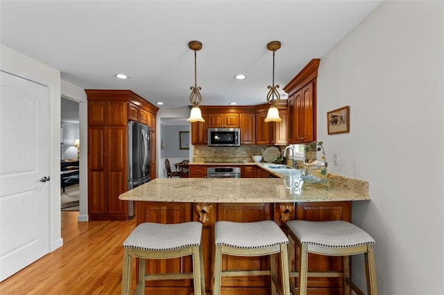 kitchen with appliances with stainless steel finishes, a sink, a peninsula, light wood-style floors, and light stone countertops