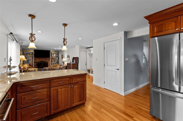 kitchen with stainless steel appliances, light wood finished floors, a fireplace, hanging light fixtures, and light stone counters