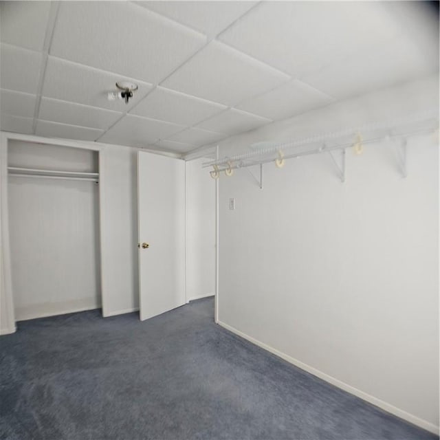 unfurnished bedroom featuring dark carpet, a paneled ceiling, a closet, and baseboards