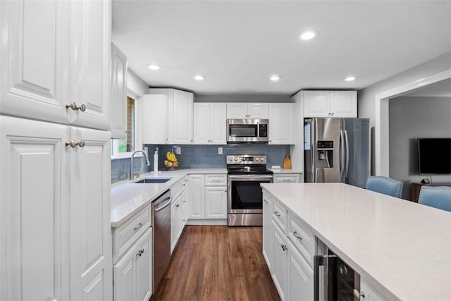 kitchen featuring appliances with stainless steel finishes, a sink, wine cooler, white cabinetry, and recessed lighting