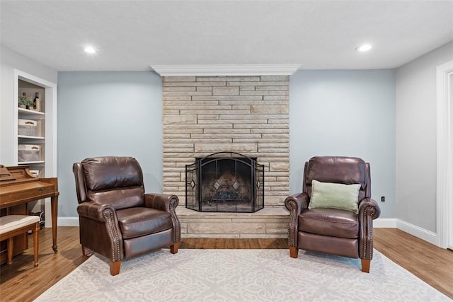 sitting room featuring wood finished floors, a stone fireplace, baseboards, recessed lighting, and built in shelves