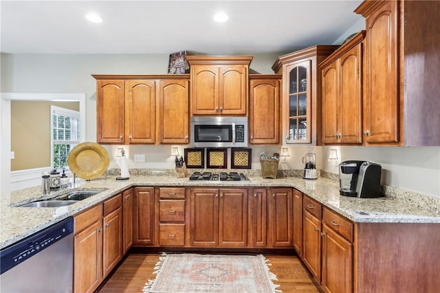 kitchen with appliances with stainless steel finishes, a sink, light wood finished floors, light stone countertops, and recessed lighting