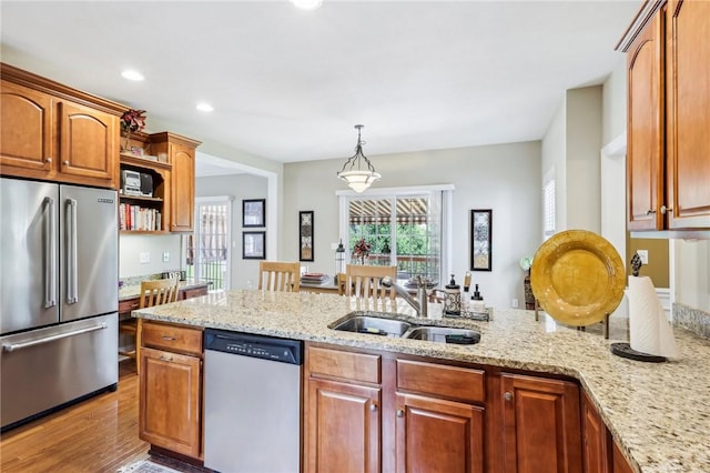 kitchen featuring stainless steel appliances, a sink, light stone counters, open shelves, and pendant lighting