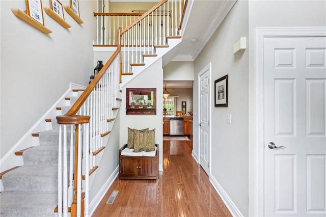 stairway featuring wood finished floors, baseboards, and crown molding