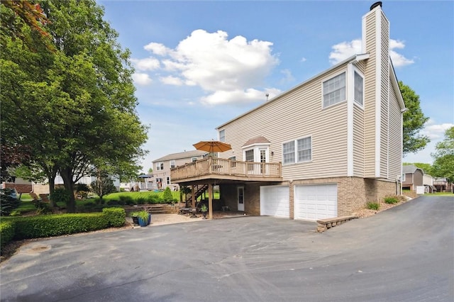 rear view of house featuring a deck, a chimney, stairway, an attached garage, and asphalt driveway