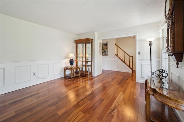 living area with wood finished floors, stairway, a wainscoted wall, and a decorative wall